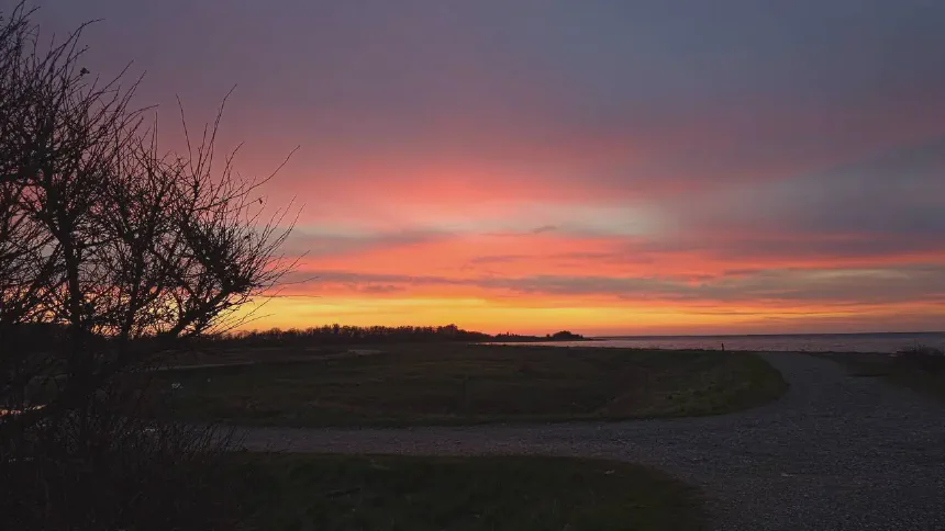 Solnedgang over en kyststrækning med rolig sø og lav horisont.